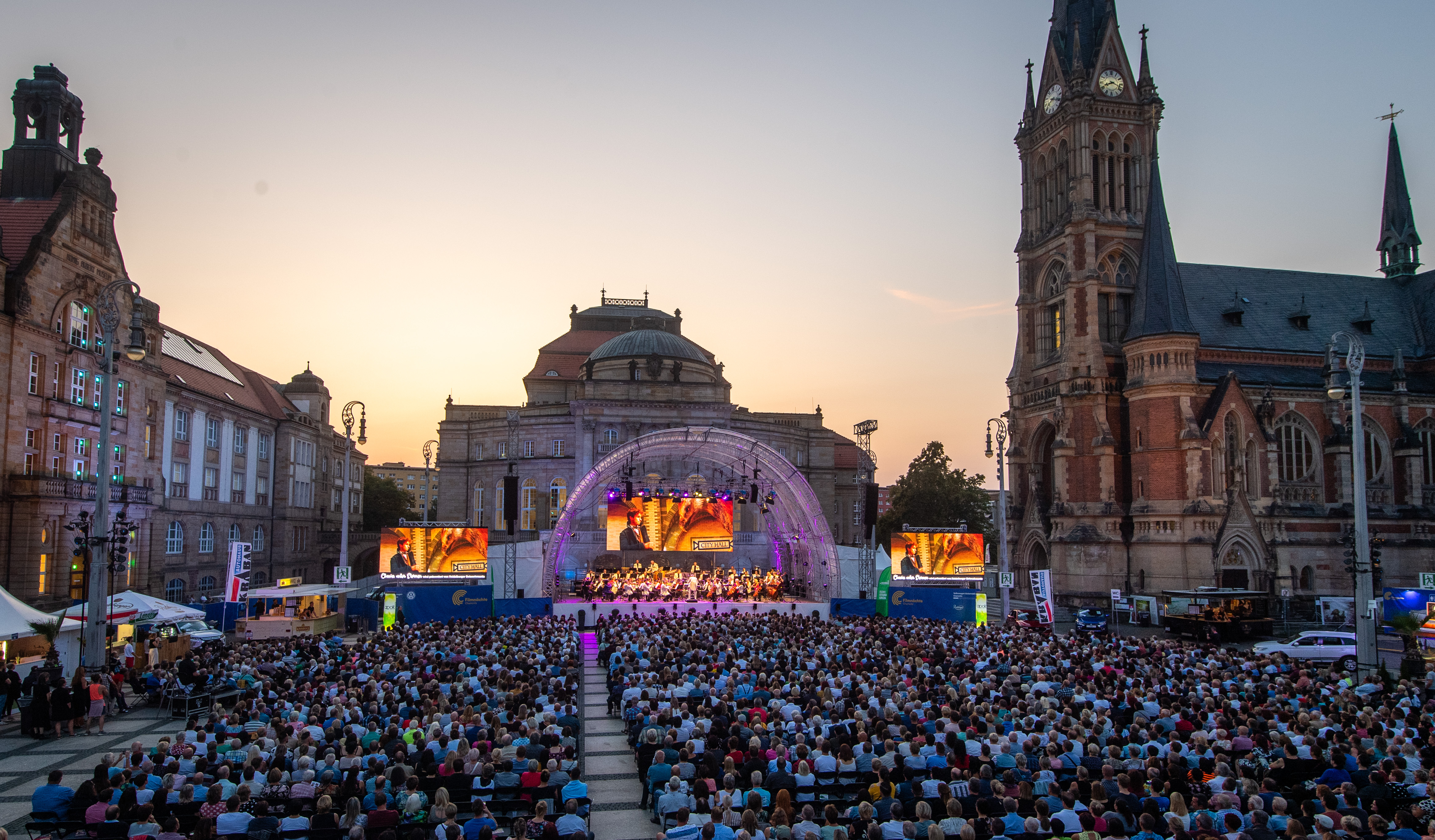 Große Bühne mit mehren LED Wänden und Lichttechnik im Hintergrund, im Vordergrund sind Menschen