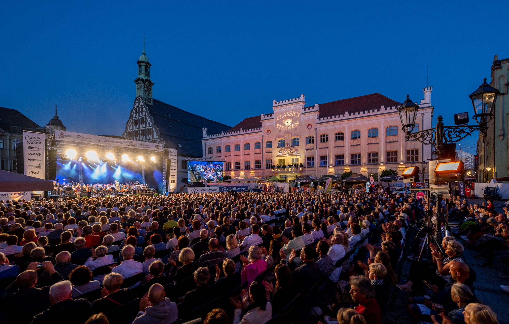 Veranstaltung, wo eine Bühne und ein beleuchtetes Gebäude im Hintergrund ist und eine Menschenmenge im Vordergrund